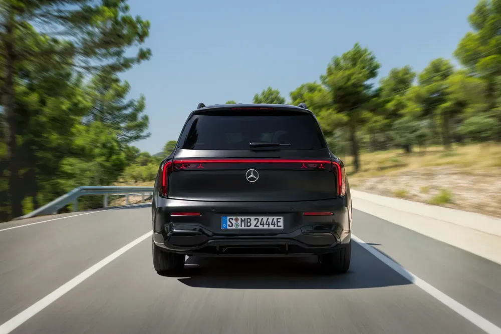 Achteraanzicht van zwarte Mercedes-Benz EQS SUV op een bosrijke weg.
