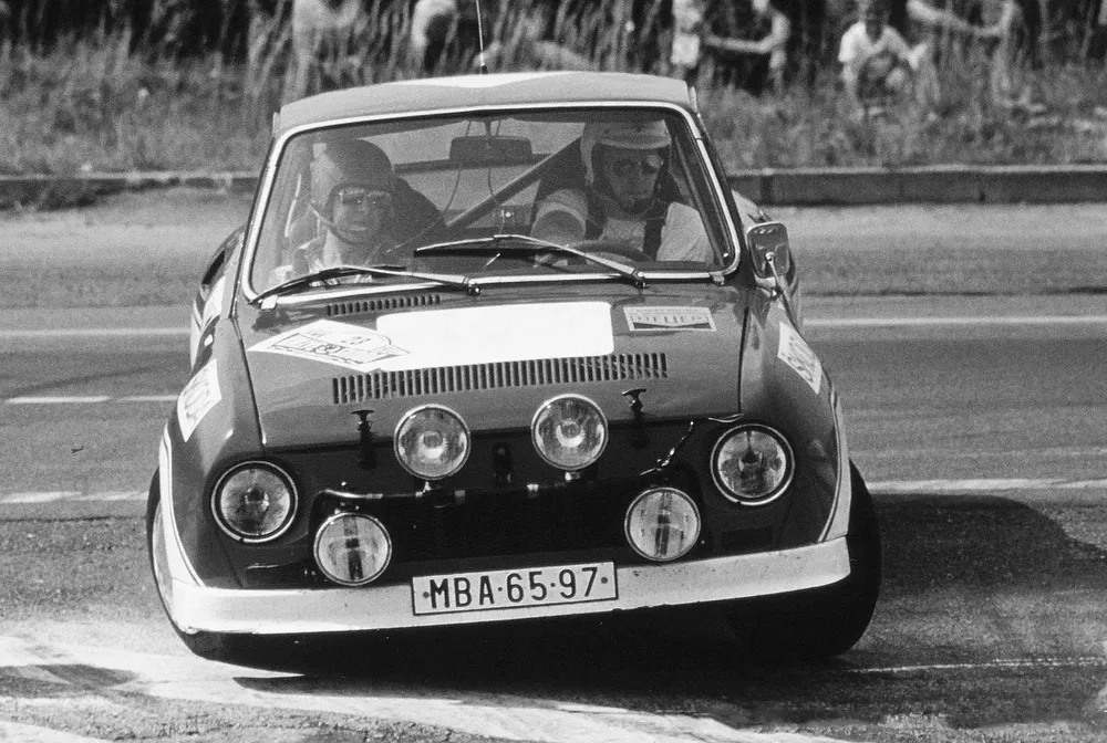 Lancia rallywagen in actie op circuit met klassieke mistlampen ingenomen.