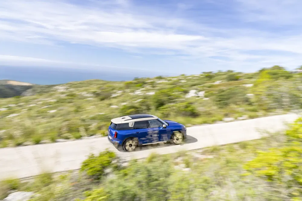SUV bleu roulant sur une route de campagne panoramique sous un ciel ensoleillé.