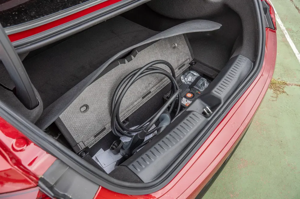 Coffre de voiture rouge avec câble de recharge pour véhicule électrique.
