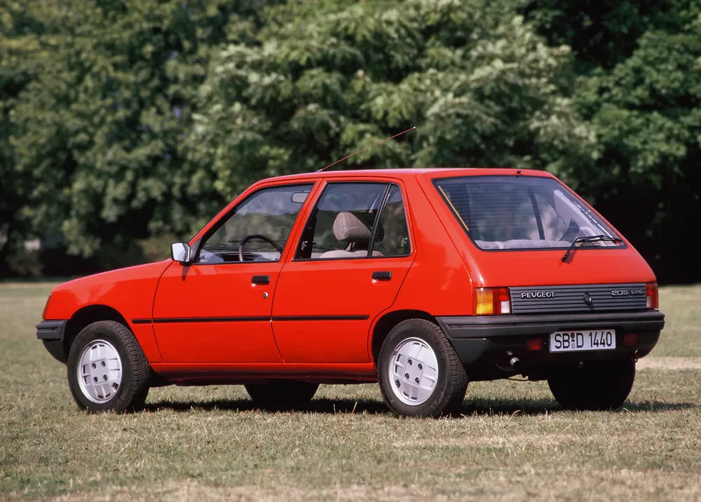 Peugeot 205 rouge sur pelouse, vue arrière dans un parc ensoleillé.