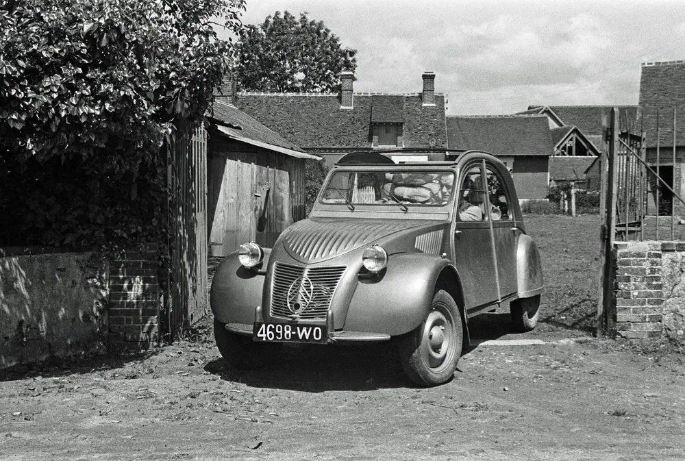 Citroën 2CV classique noir et blanc dans un cadre rural ancien.