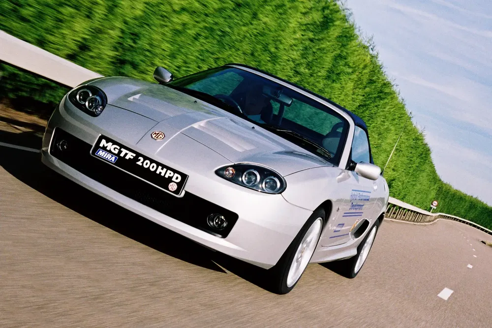 {"fr":"Voiture MG TF 200 HP à haute performance roulant sur une route bordée de haies.","nl":"Presterende MG TF 200 HP op een weg omgeven door groene heggen."}