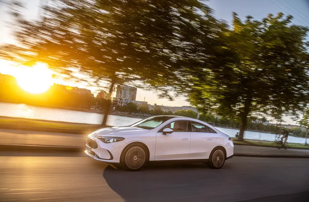 Witte luxe auto rijdt bij zonsondergang langs een rivier.