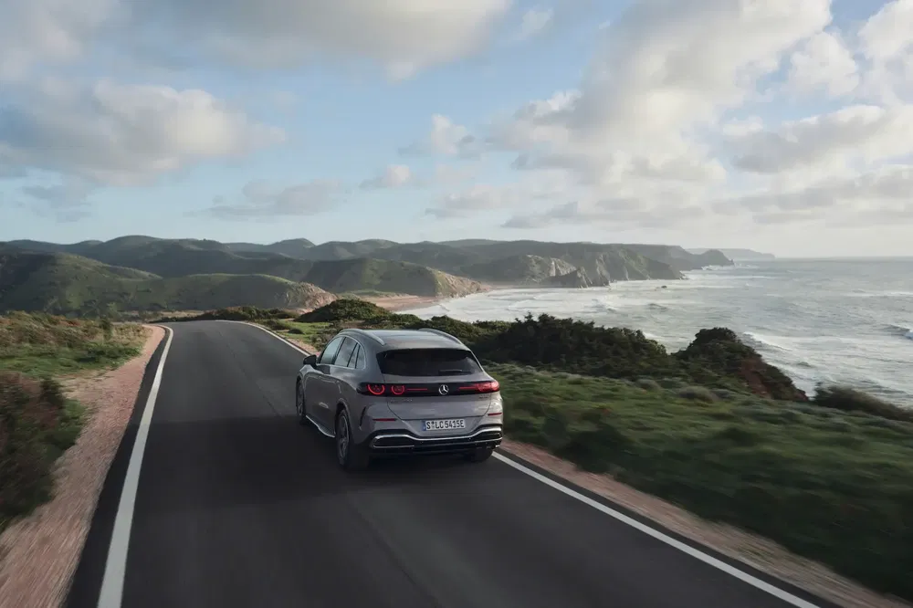 Mercedes-Benz EQE SUV grise sur route côtière avec vue sur l'océan et les collines.