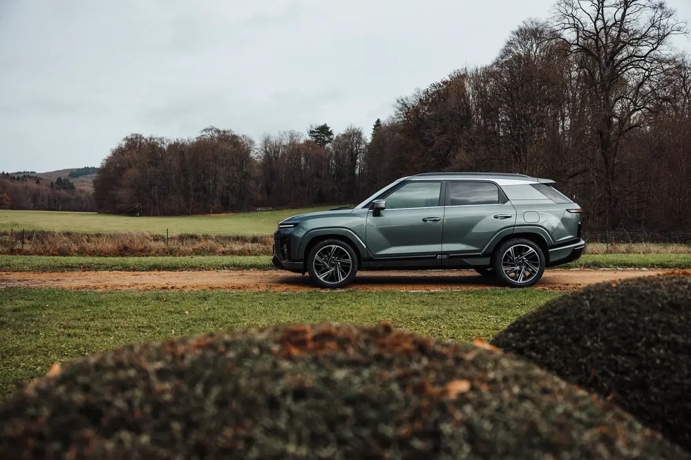 Moderne SUV geparkeerd op landweg, omringd door bomen in de winter.