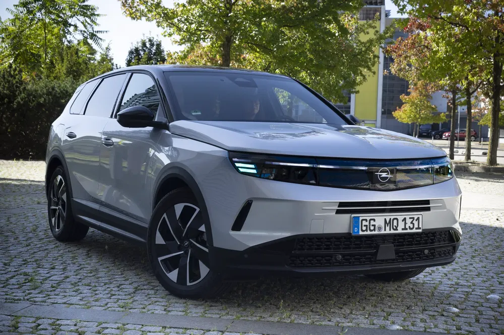 {"fr":"SUV Opel blanc, design moderne, stationné sur pavé sous des arbres ensoleillés.","nl":"Witte Opel SUV, modern ontwerp, geparkeerd op straatstenen onder zonnige bomen."}