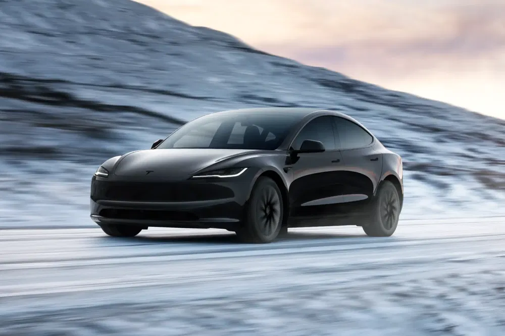Tesla Model 3 noire roulant sur une route enneigée au crépuscule.