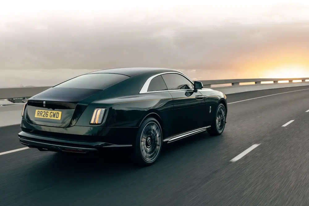 Rolls-Royce coupé noir roulant sur une autoroute au coucher du soleil.