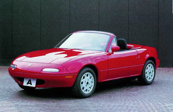 Mazda MX-5 rouge, cabriolet emblématique, stationné sur pavé devant mur sombre.