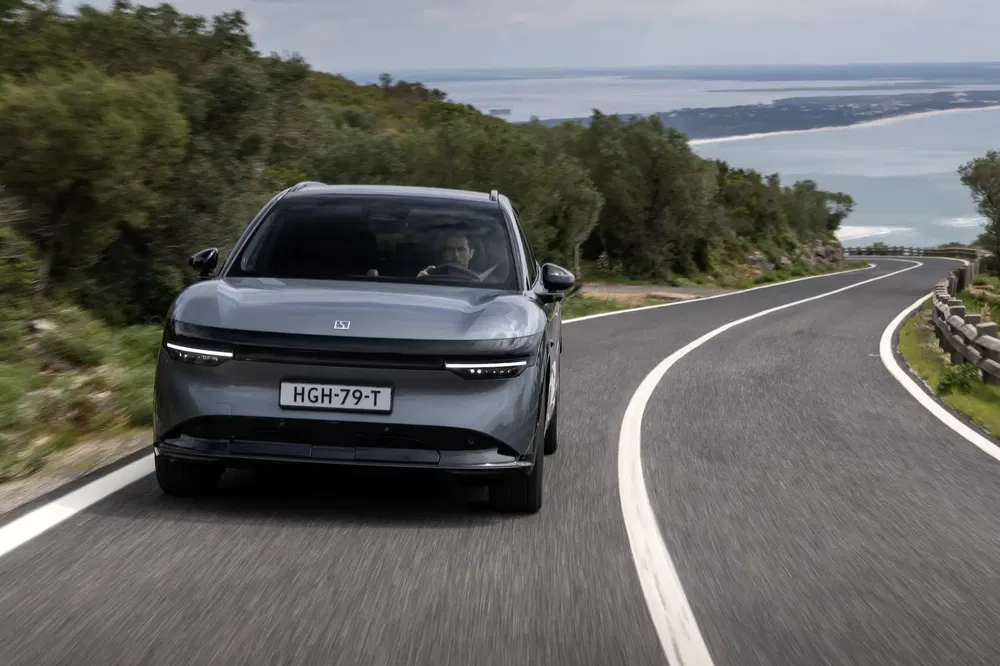 Voiture électrique roulant sur route côtière sinueuse avec paysage océanique en arrière-plan.