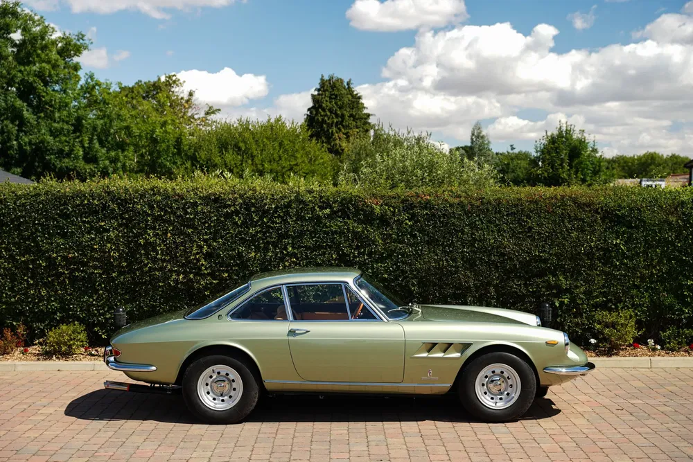 Ferrari 275 GTB classique verte garée sur une allée pavée par une journée ensoleillée.