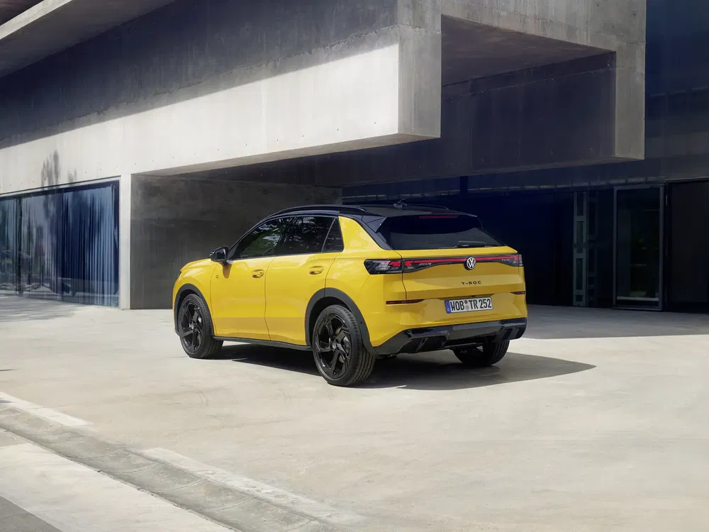 Gele Volkswagen T-Roc met zwart dak, geparkeerd voor een modern gebouw.