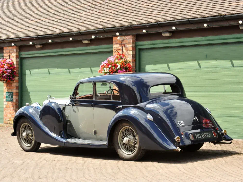Bentley classique garée devant des garages verts, design élégant et vintage.