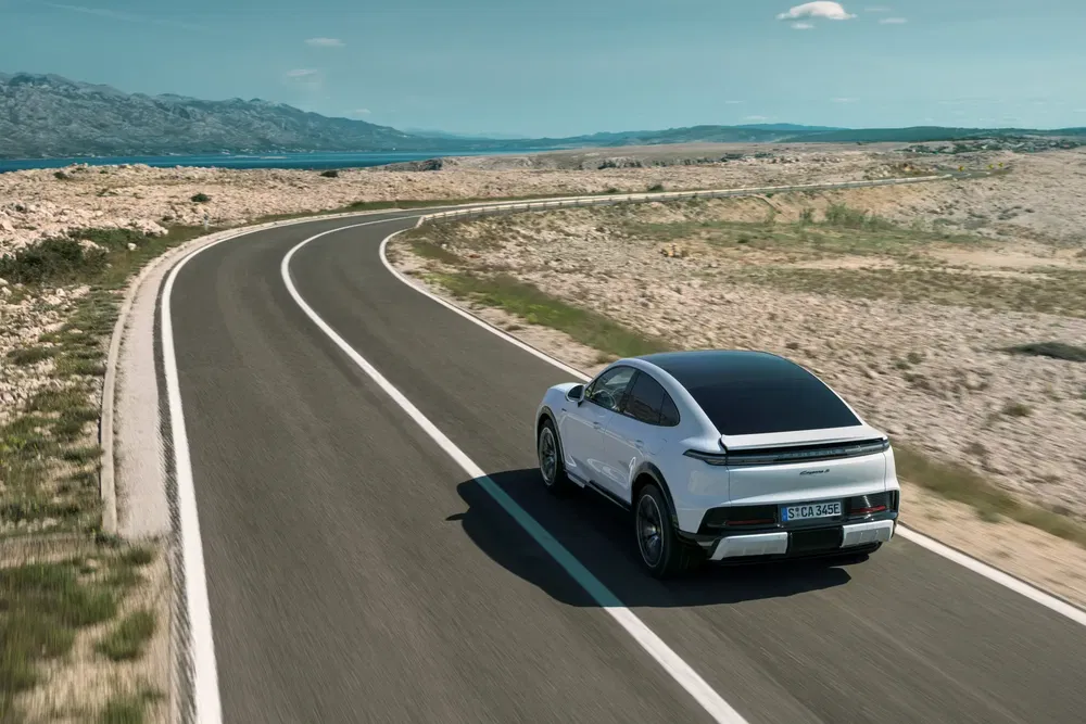 Porsche Taycan op kronkelige kustweg bij zonnig weer, met elegant en sportief ontwerp.