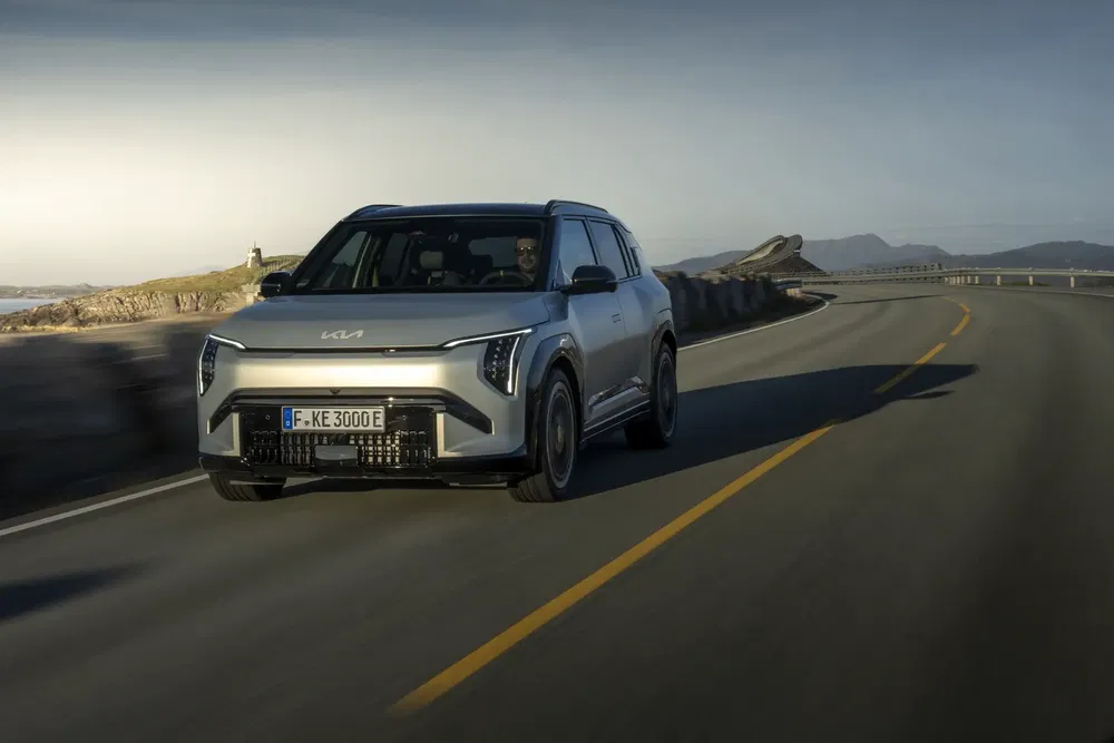 Kia EV9 électrique roulant sur une route côtière sinueuse avec paysage montagneux.