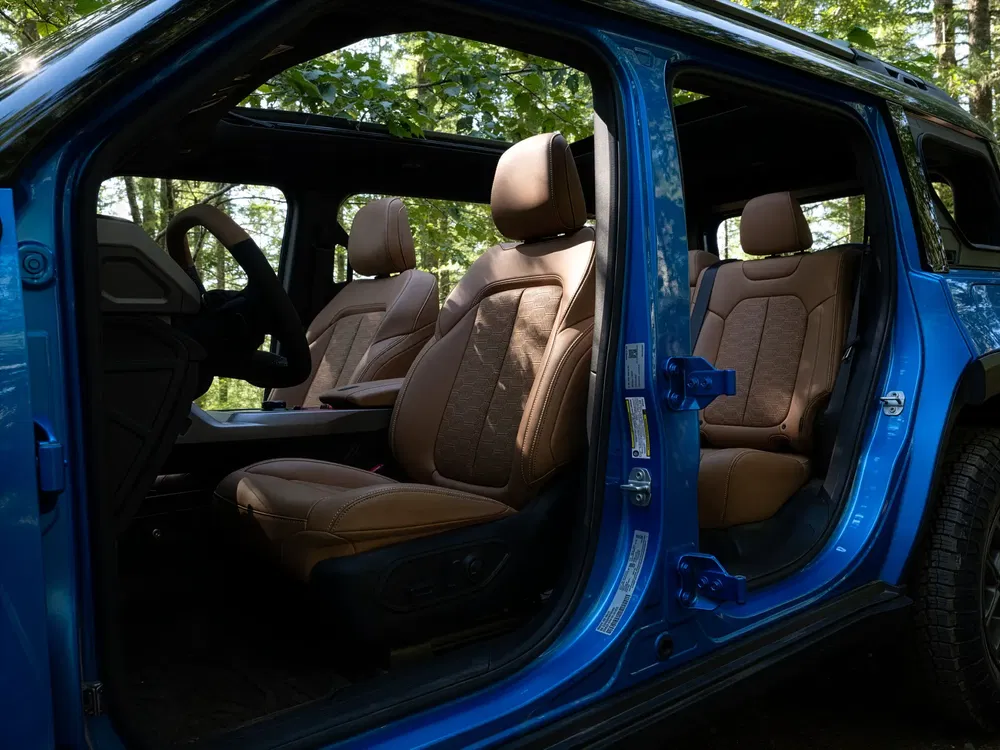 Interieur van een elektrische SUV met bruine lederen stoelen, deuren open in het bos.