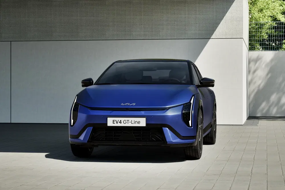 Blauwe elektrische Kia EV4 GT-Line geparkeerd voor een moderne muur.