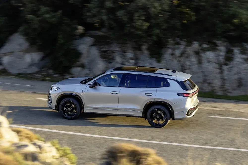 Zilveren BMW iX op kronkelige weg met rotsachtig landschap en begroeiing.