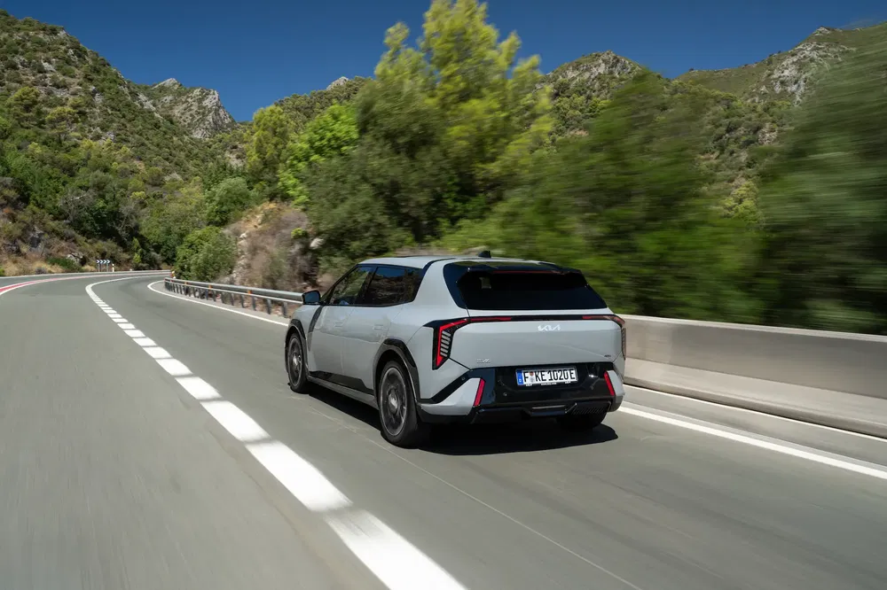Kia EV en virage sur une route montagneuse, encadrée par une végétation luxuriante.