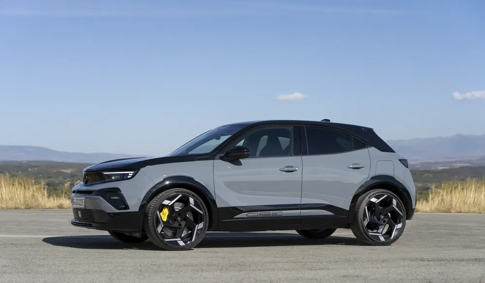 Grijze Opel Mokka geparkeerd, zijaanzicht, zwarte velgen, heldere lucht op de achtergrond.