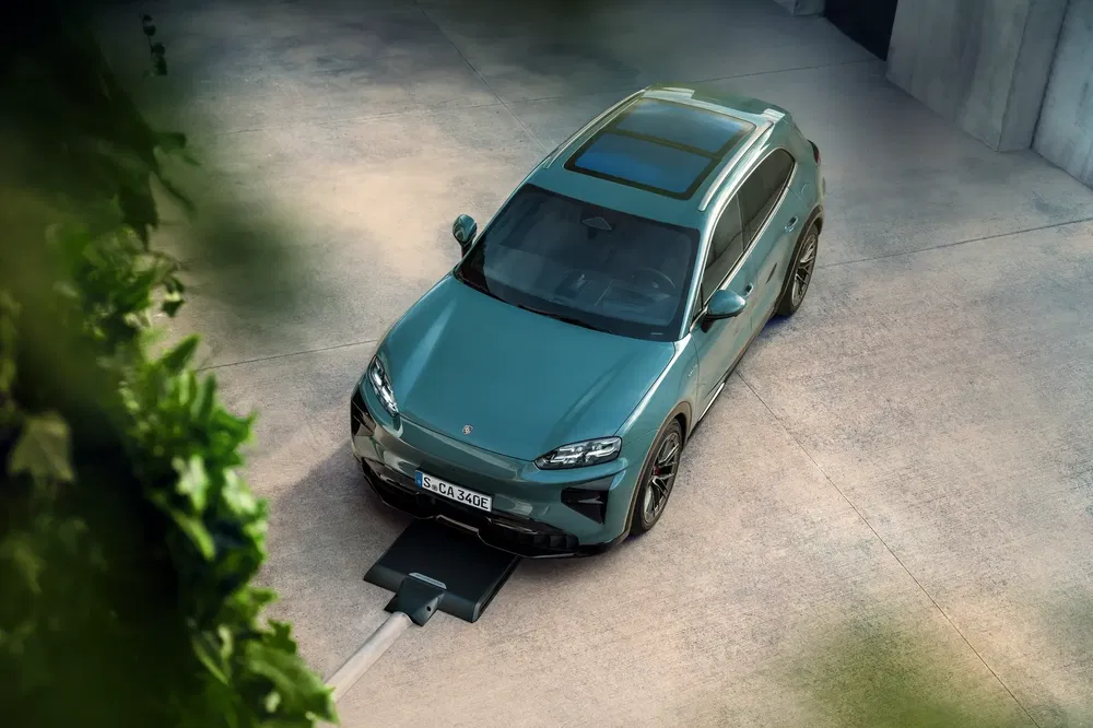 De groene elektrische Porsche Macan laadt draadloos op in een moderne oprit.