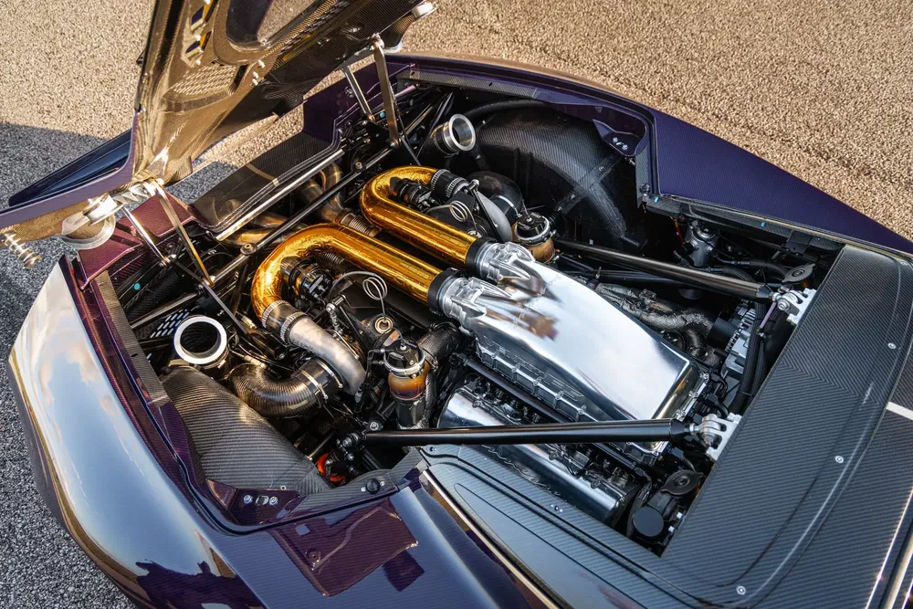 Sportauto motor met gouden buizen en glanzend chroom, open motorkap buiten.