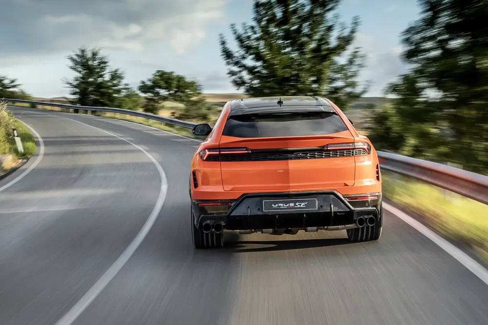 Oranje Lamborghini Urus op kronkelige weg met groene achtergrond.