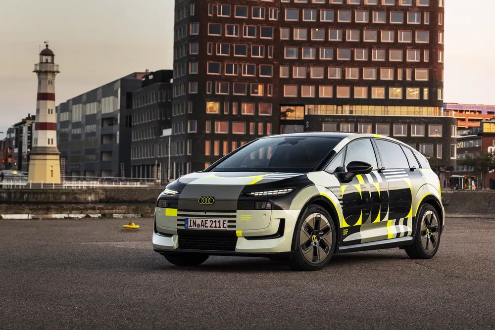 Concept car Audi Q6 e-tron stationné devant un bâtiment industriel et un phare.