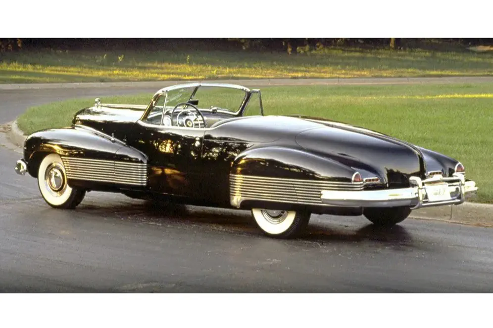Buick Y-Job cabriolet vintage sur route, extérieur noir brillant et pneus à flancs blancs.