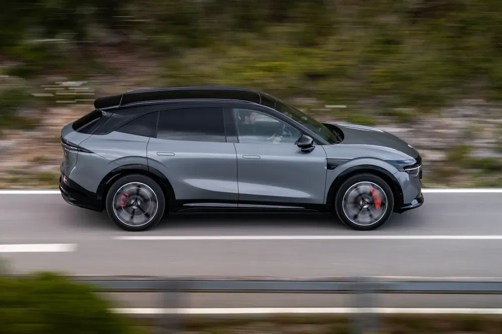 Voiture électrique Byton électrique gris foncé roulant sur route bordée de verdure.