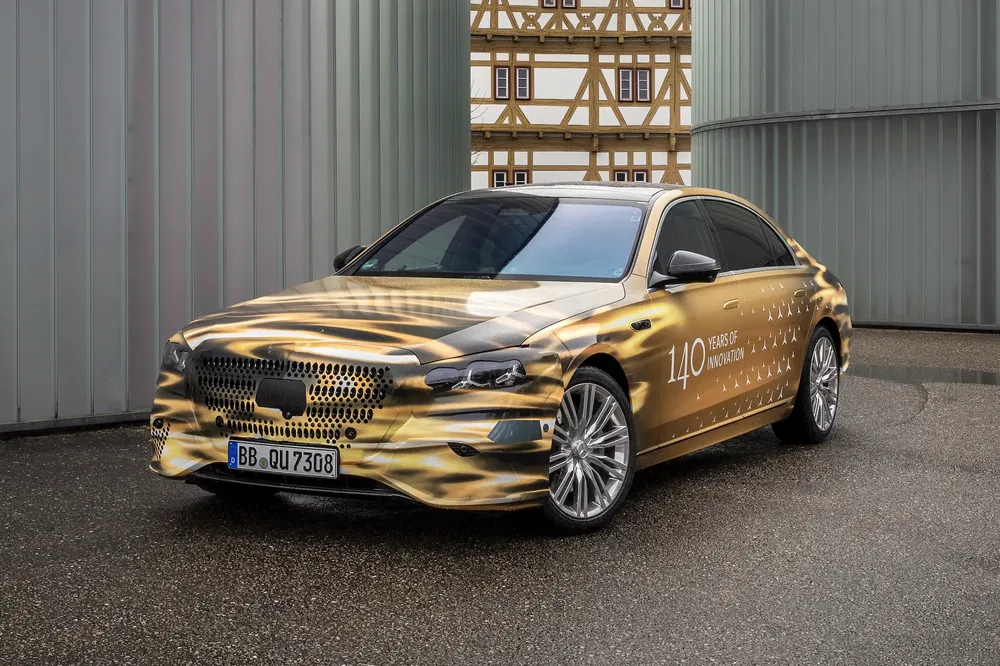 Mercedes-Benz hybride dorée, design camouflage pour 140 ans d'innovation, stationnée devant bâtiments.