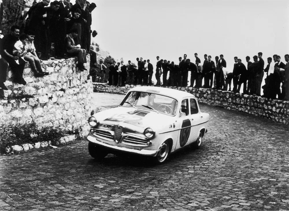 Voiture de course Alfa Romeo sur route pavée, spectateurs alignés sur le bord.