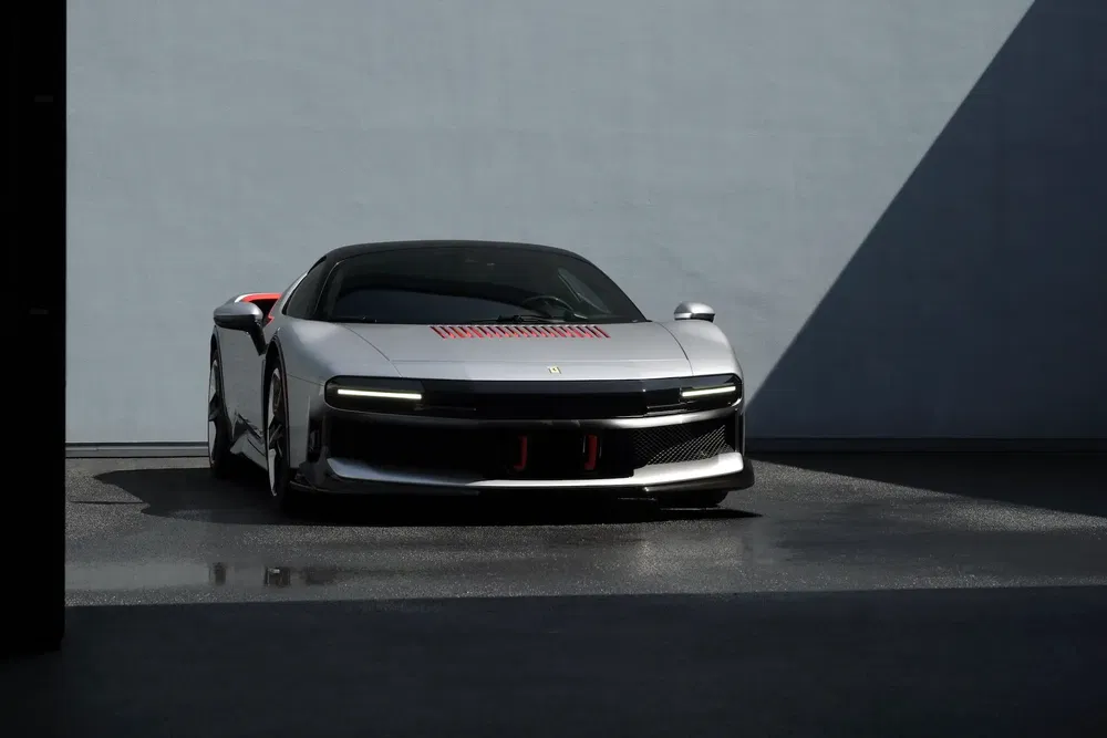 Moderne zilveren Ferrari geparkeerd buiten tegen een minimalistische grijze achtergrond.