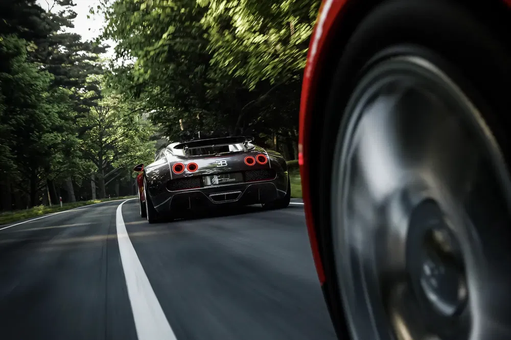 Bugatti Veyron roulant sur route bordée d'arbres avec roue avant floue au premier plan.