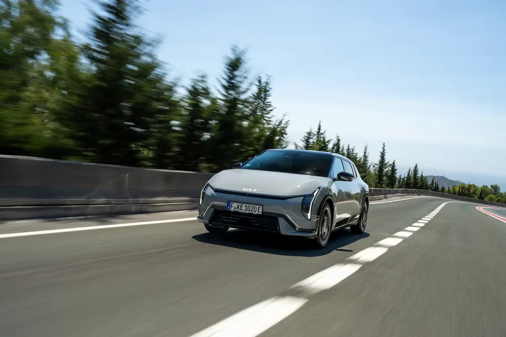 Kia EV6 argentée roulant sur autoroute bordée d'arbres par journée ensoleillée.