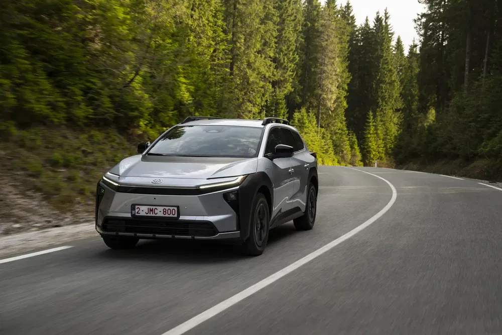 Toyota bZ4X argent roulant sur une route sinueuse bordée de forêt verdoyante.
