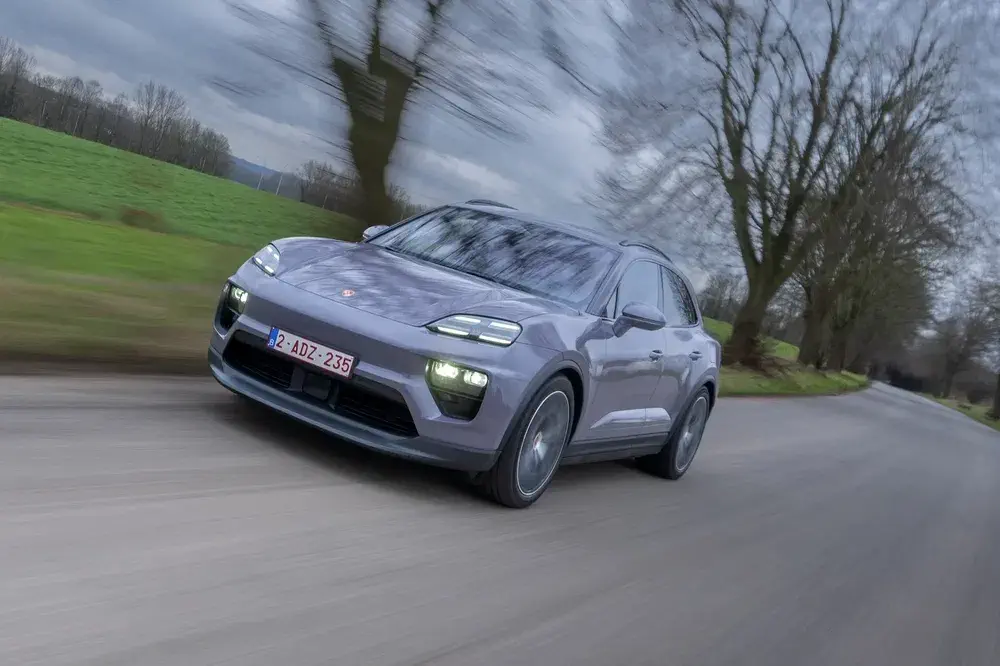 Porsche Macan roulant vite sur une route de campagne bordée d'arbres en hiver.