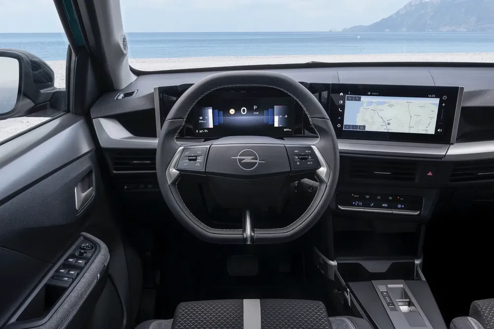 Intérieur de l'Opel Astra avec tableau de bord numérique et écran tactile, vue sur plage.