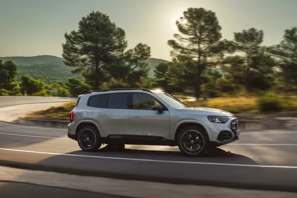 SUV moderne Mercedes-Benz GLB roulant sur une route bordée d'arbres au coucher du soleil.