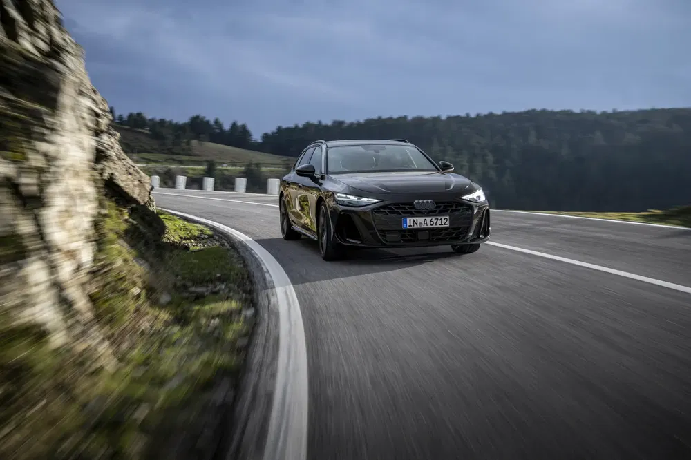 Audi noire en conduite sur route de montagne sinueuse par temps nuageux.