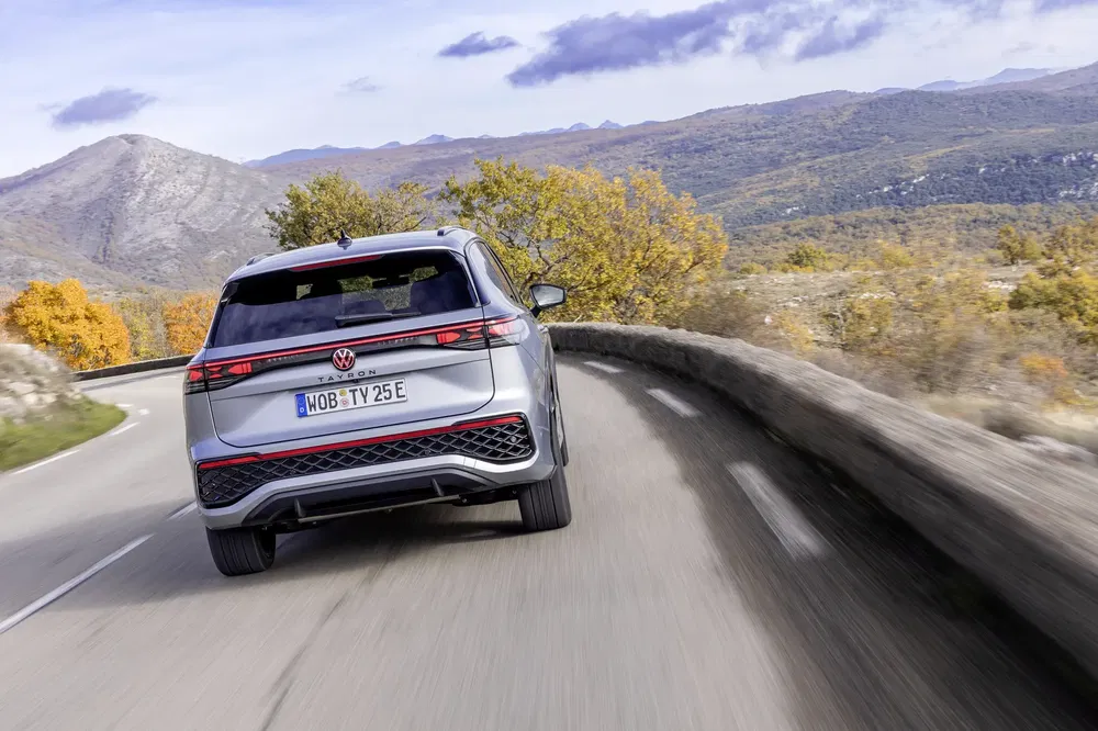 Volkswagen ID.4 rijdt op een bochtige weg met herfstlandschap en bergen op de achtergrond.