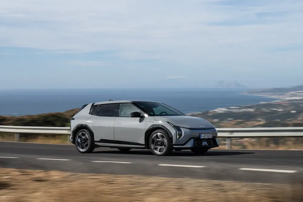SUV électrique Kia EV9 sur route côtière avec vue sur l'océan et paysage pittoresque.