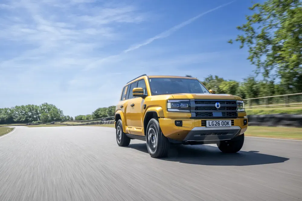 Gele Denza BAO 5 SUV rijdt op zonnige weg met blauwe lucht en bomen op achtergrond.