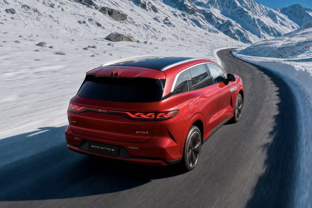 BYD Atto 3 rouge roulant sur route enneigée, montagnes en arrière-plan.