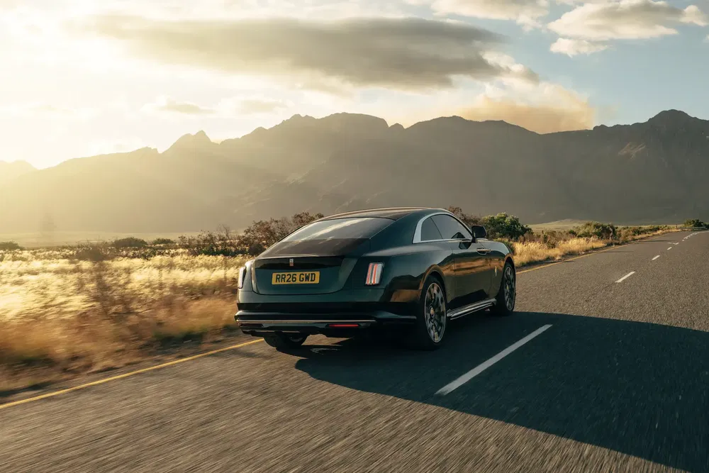 Rolls-Royce coupé sur route de campagne au coucher du soleil avec montagnes en arrière-plan.