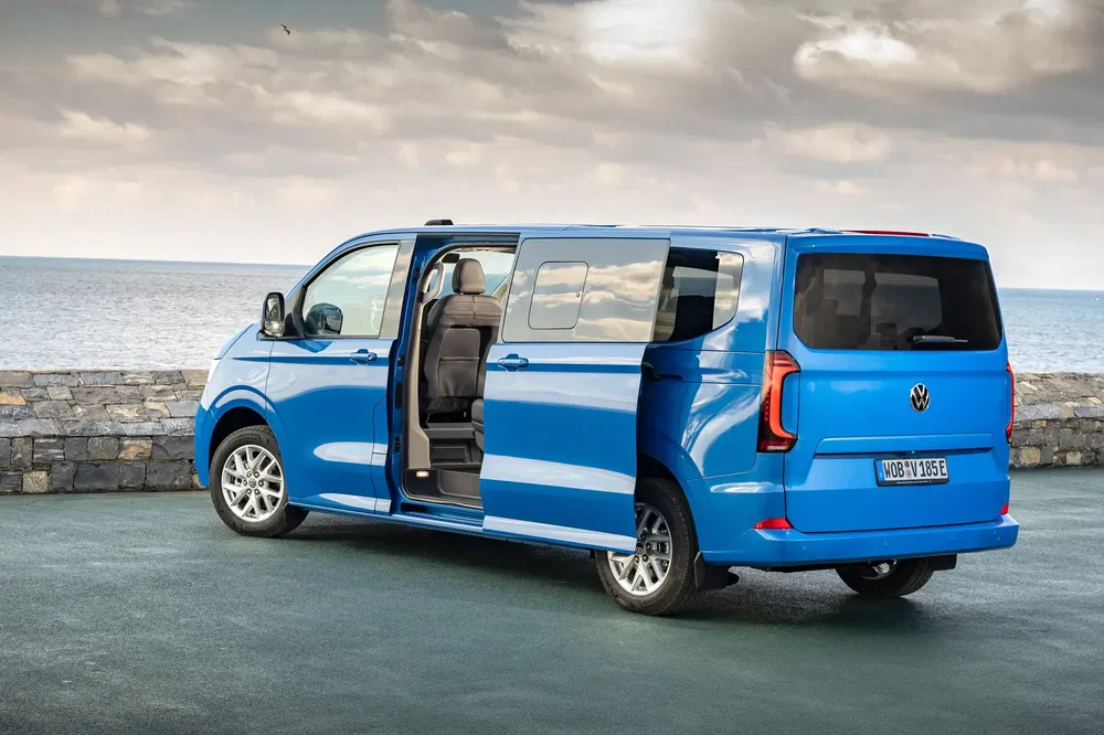 Blauwe Volkswagen Multivan met open deur aan kustlijn, bewolkte hemel, reissfeer.