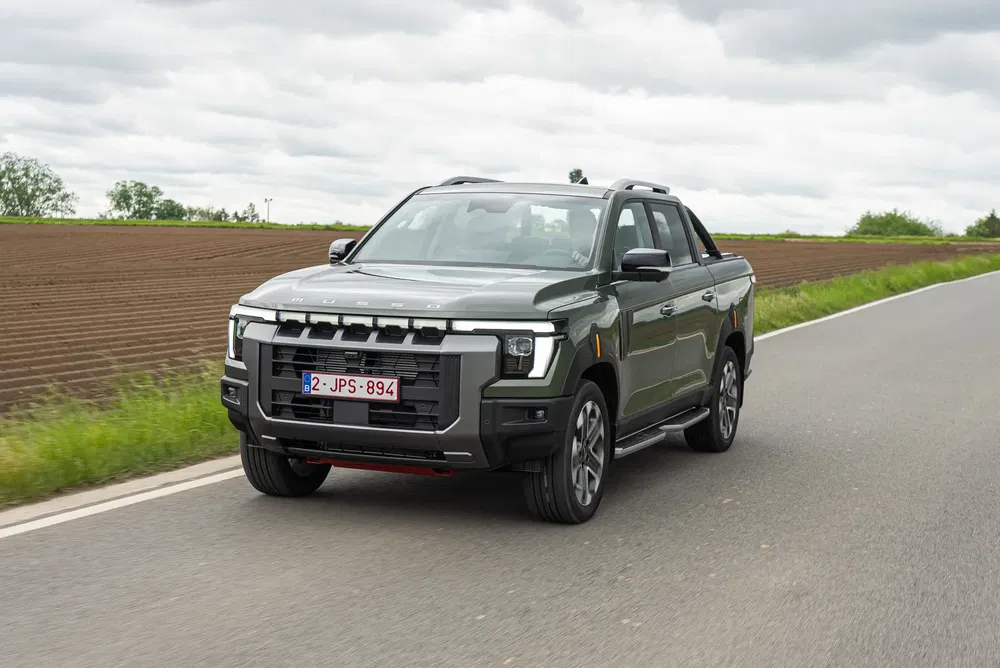 Pickup moderne roulant sur une route de campagne, ciel nuageux en arrière-plan.