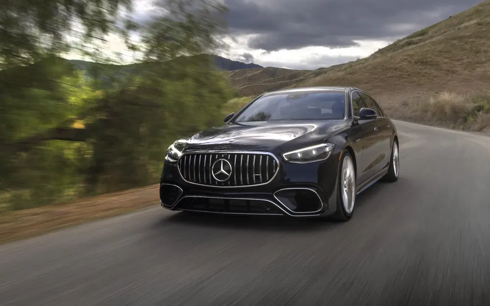 Mercedes S-Class noire roulant sur une route sinueuse, paysage montagneux en arrière-plan.