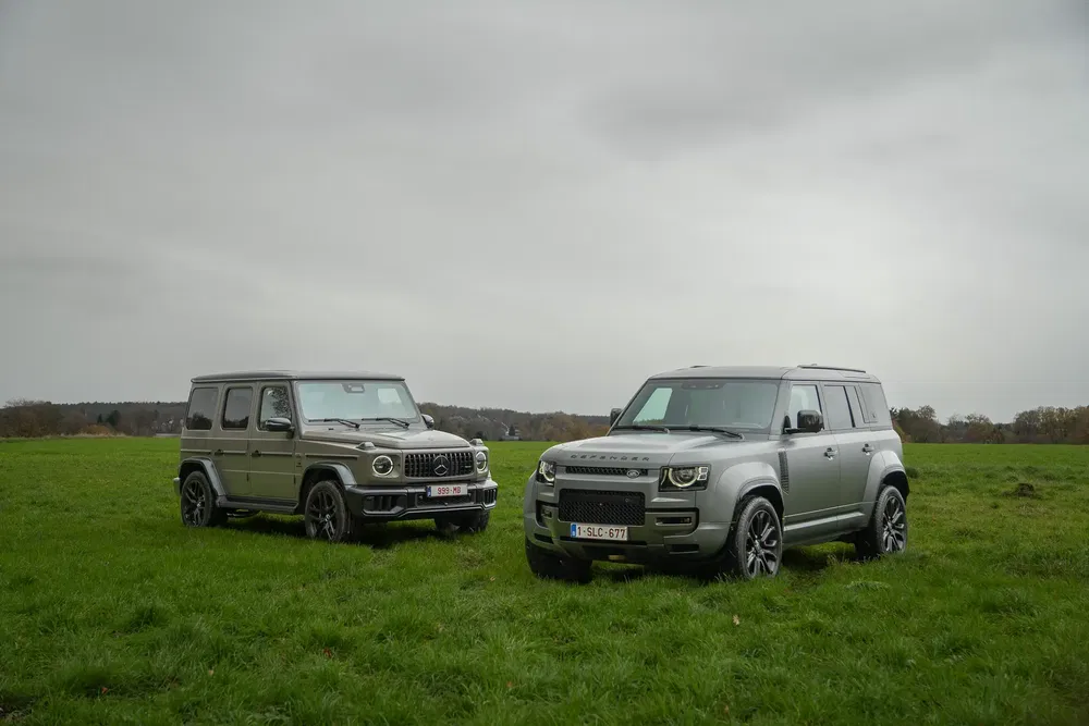 Mercedes-Benz G-Class et Land Rover Defender stationnés dans un champ, ciel nuageux.